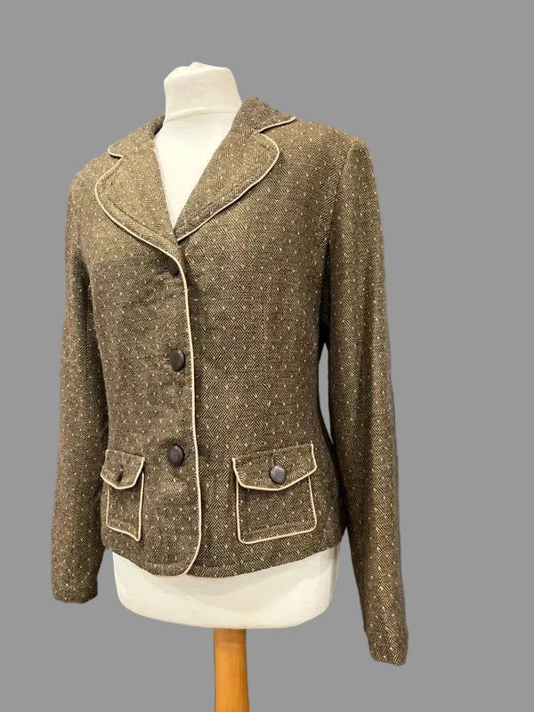 A brown tweed blazer jacket with beige contrast piping and dark buttons, displayed on a white mannequin torso against a gray paneled wall.