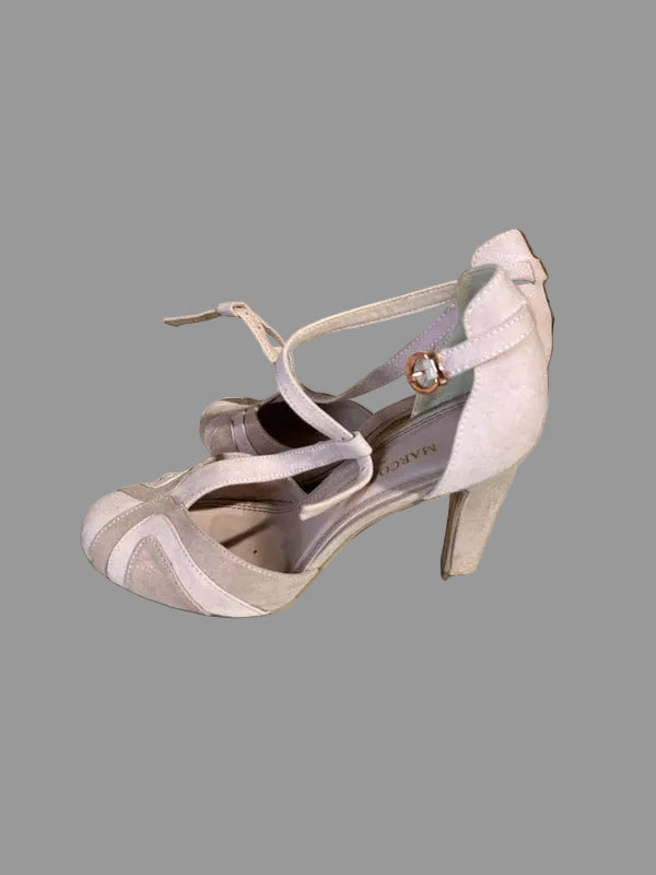 A pair of light pink high-heeled pumps with slingback straps and ankle ties, photographed on a light tiled floor in front of a wooden step.
