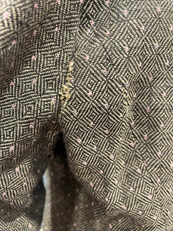 Close-up of a textured woven fabric with a geometric diamond pattern in black, beige, and light pink, featuring a central gold-toned zipper.