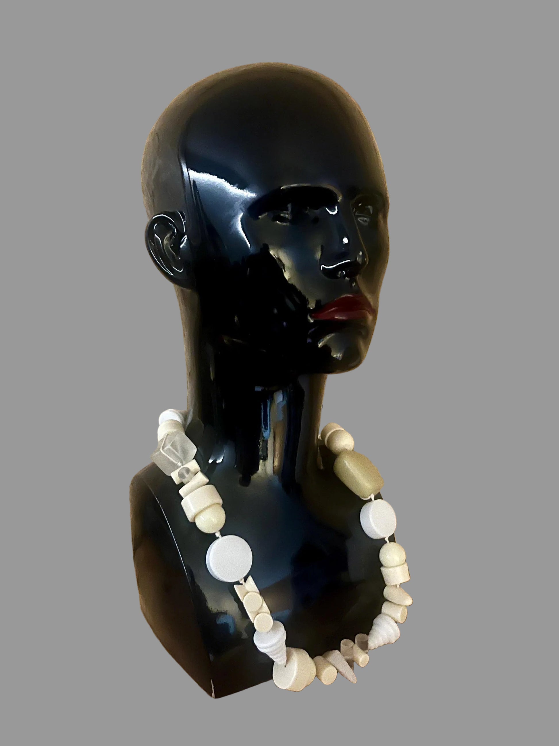 Black mannequin head with a white beaded necklace against a wooden background