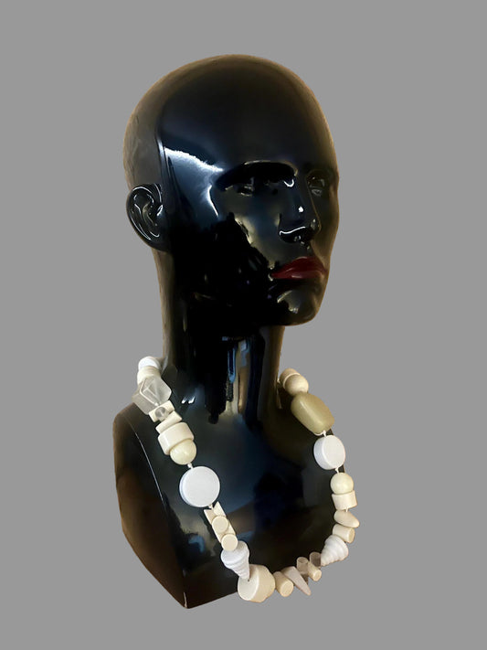 Black mannequin head with a white beaded necklace against a wooden background